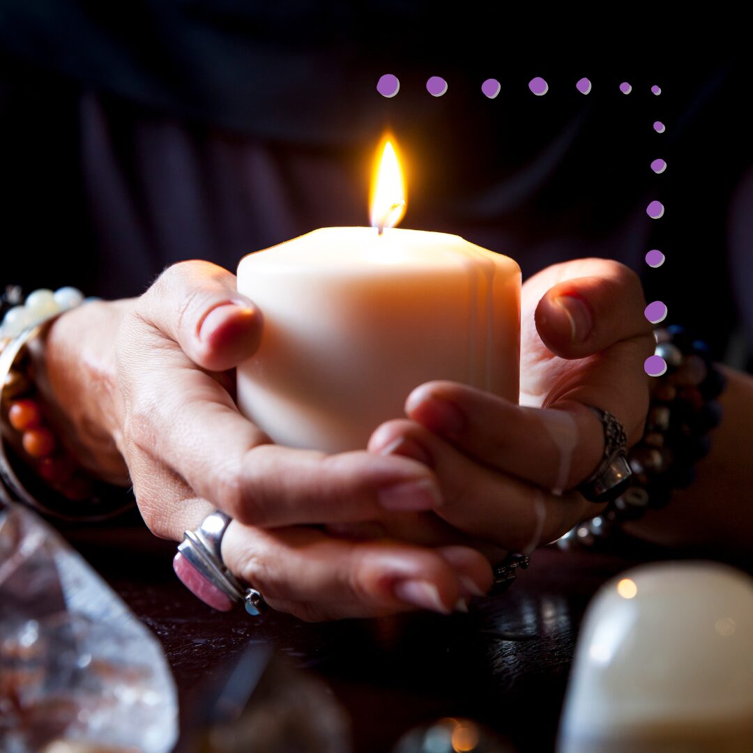 Two hands loosely holding a lit white pillar candle for Wiccan Rede meditation.