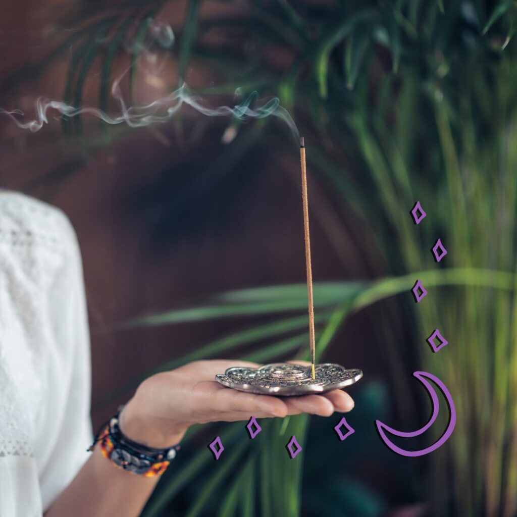 a hand holding an incense burner with a lit stick of incense trailing smoke