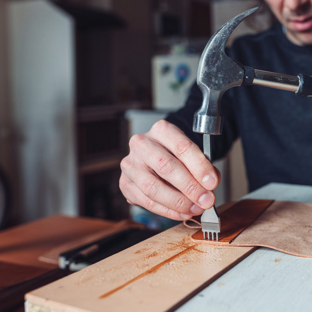 hands holding a leather punch and a hammer, poised to strike