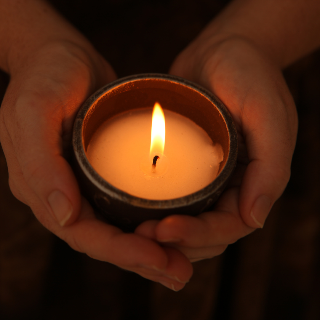 two hands holding a cup with a lit candle