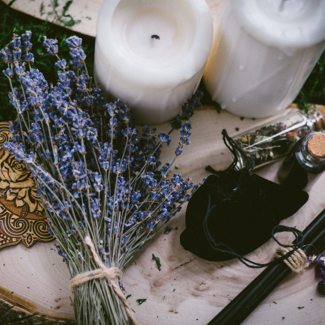 a tied bunch of lavender, some candles, a black velvet looking pouch, small glass jars with herbs